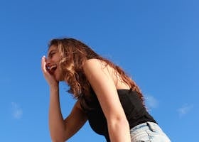 A young woman in casual attire laughing outdoors against a vibrant blue sky, radiating happiness.